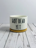 White pot with 'Not Dead Yet' text on a wooden surface