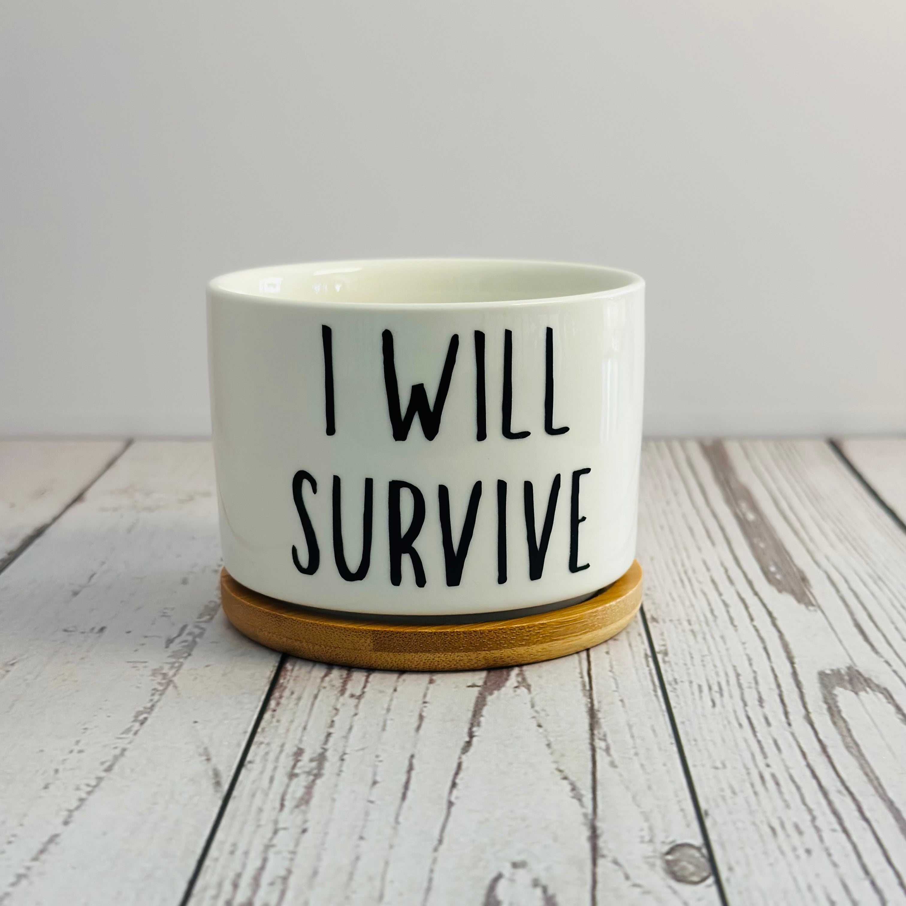 White ceramic pot with 'I Will Survive' text on a wooden surface