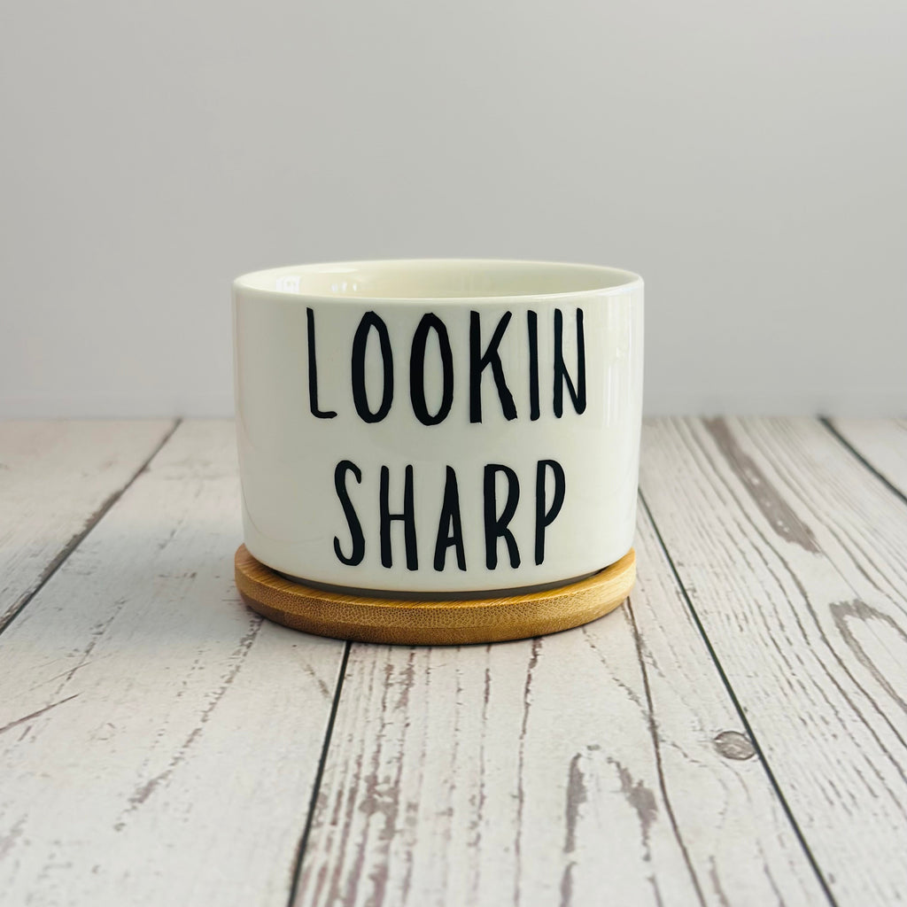 White pot with 'LOOKIN SHARP' text on a wooden surface