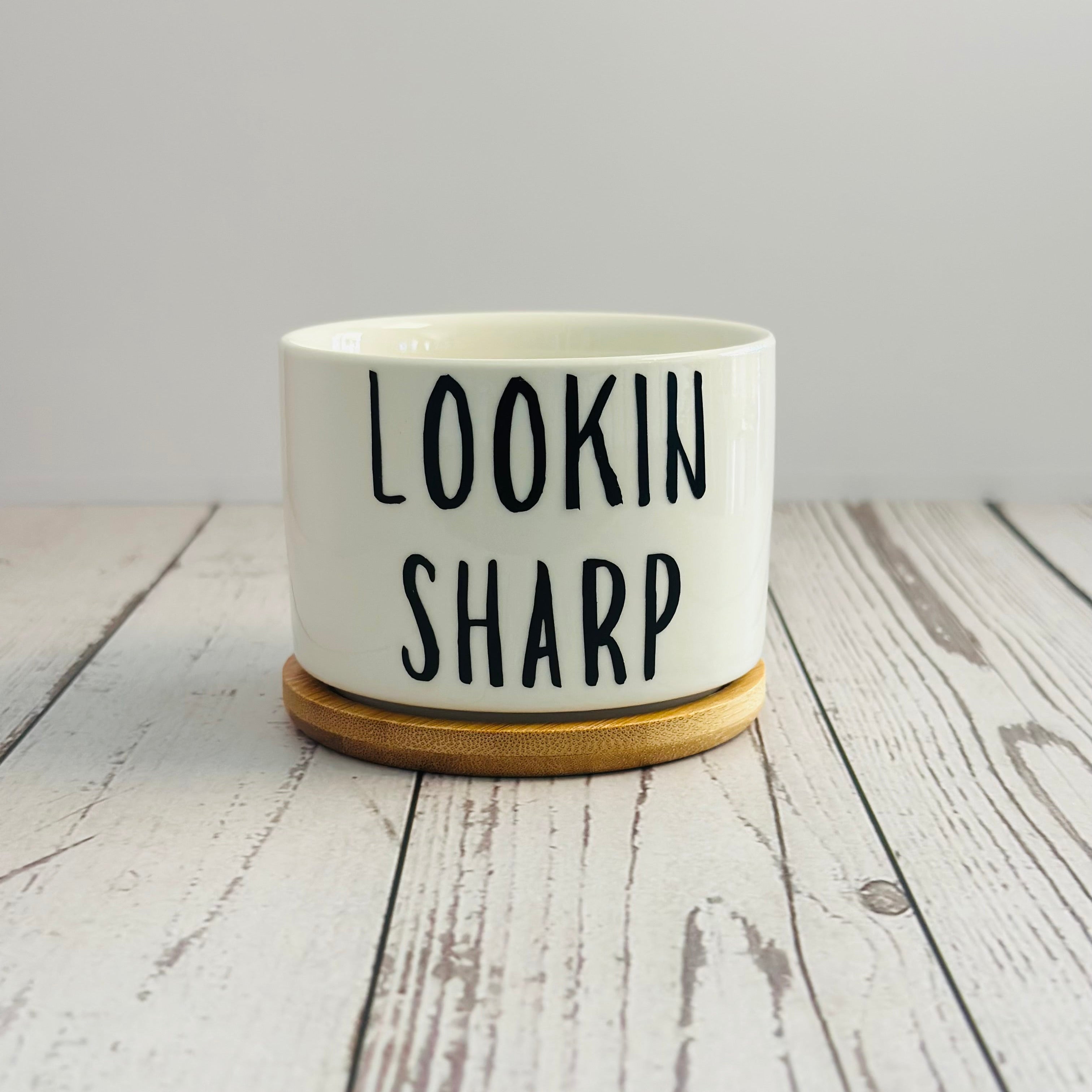 White pot with 'LOOKIN SHARP' text on a wooden surface