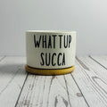 White container with 'WHAT UP SUCCA' text on a wooden surface