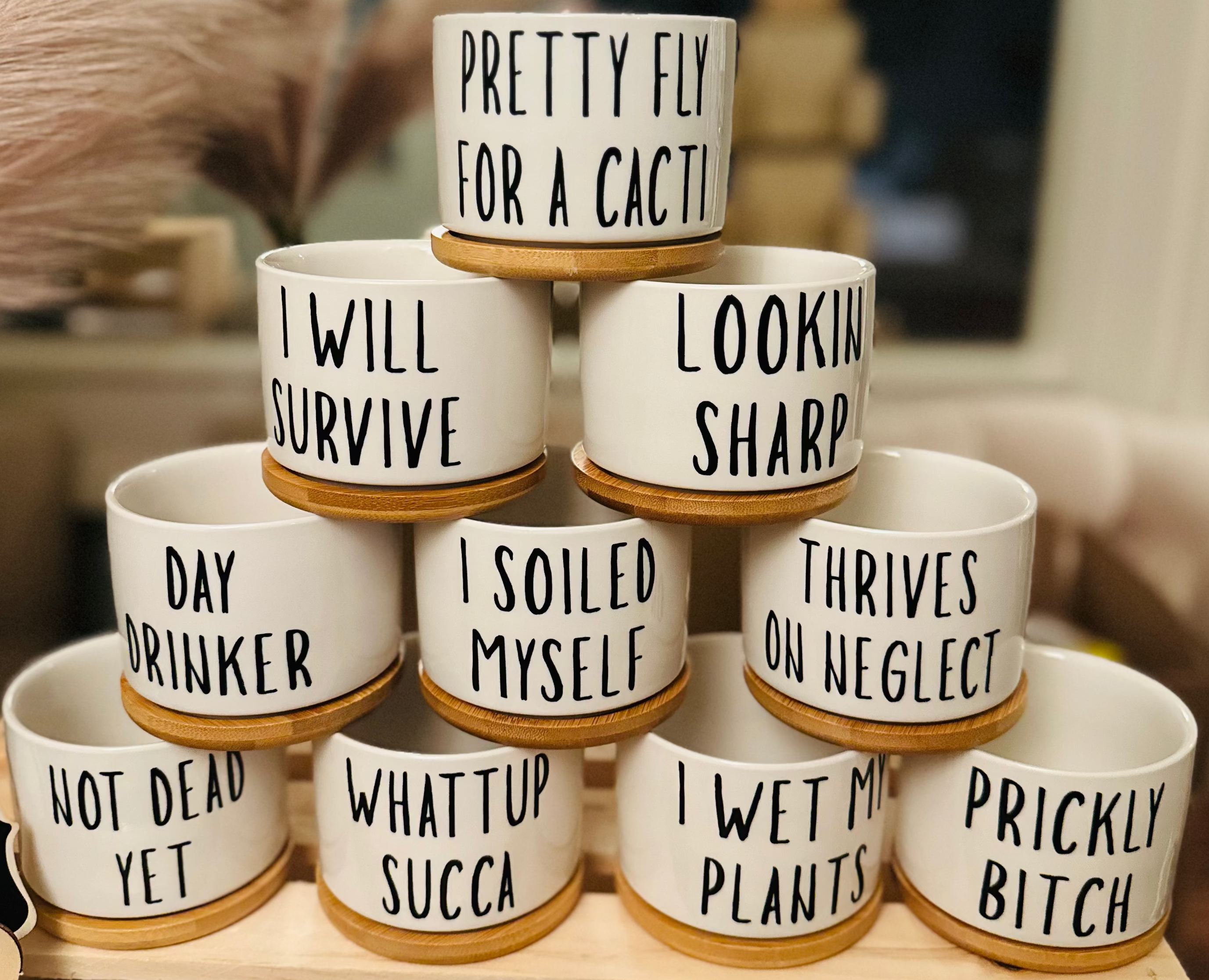 Stack of white ceramic pots with humorous text on a wooden stand.